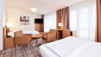 Habitación de hotel con cama, dos sillones, una mesita redonda, escritorio, televisión y un amplio ventanal con cortinas.