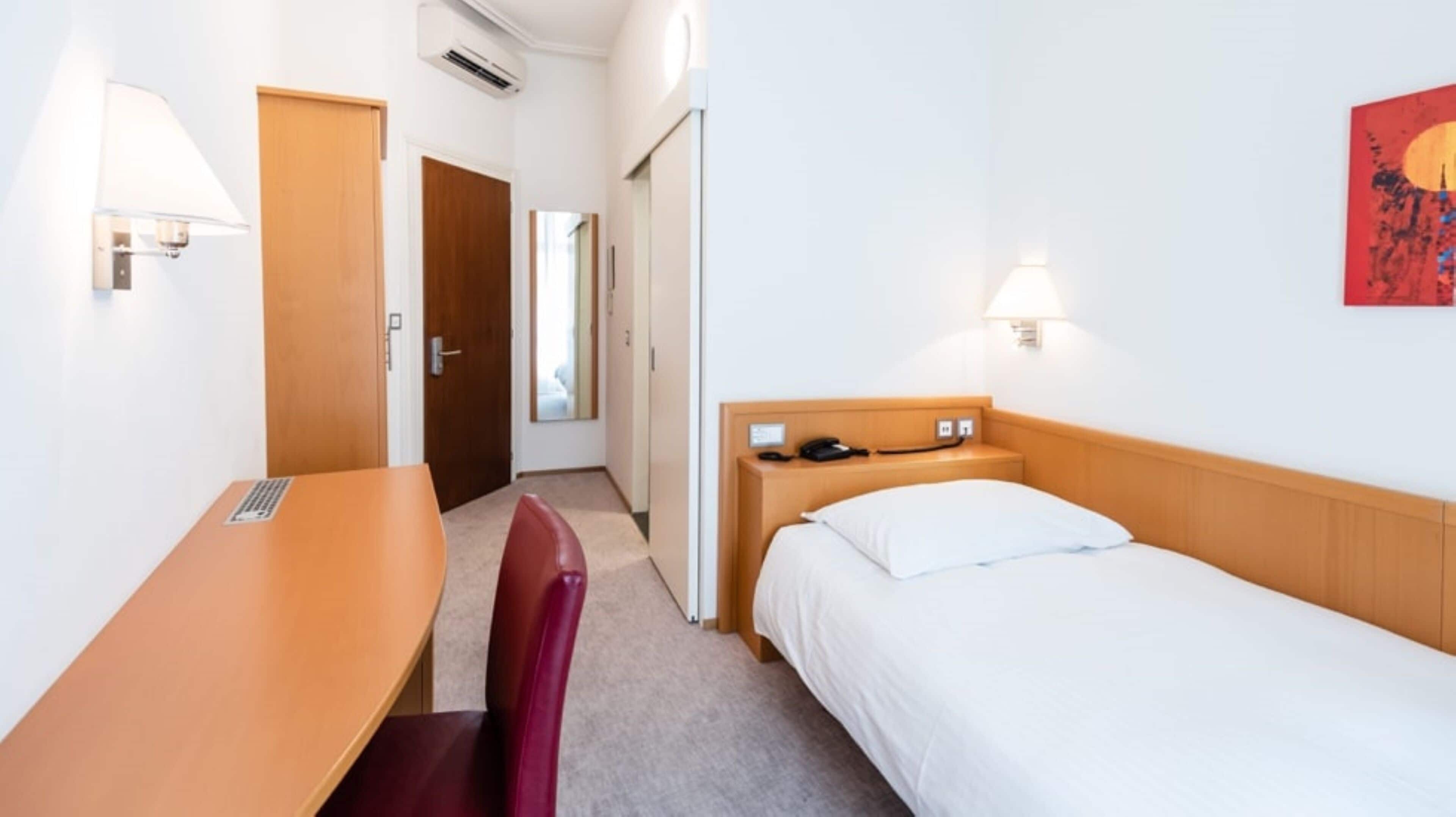 A hotel room with a single bed, a desk, a chair, and a small table.