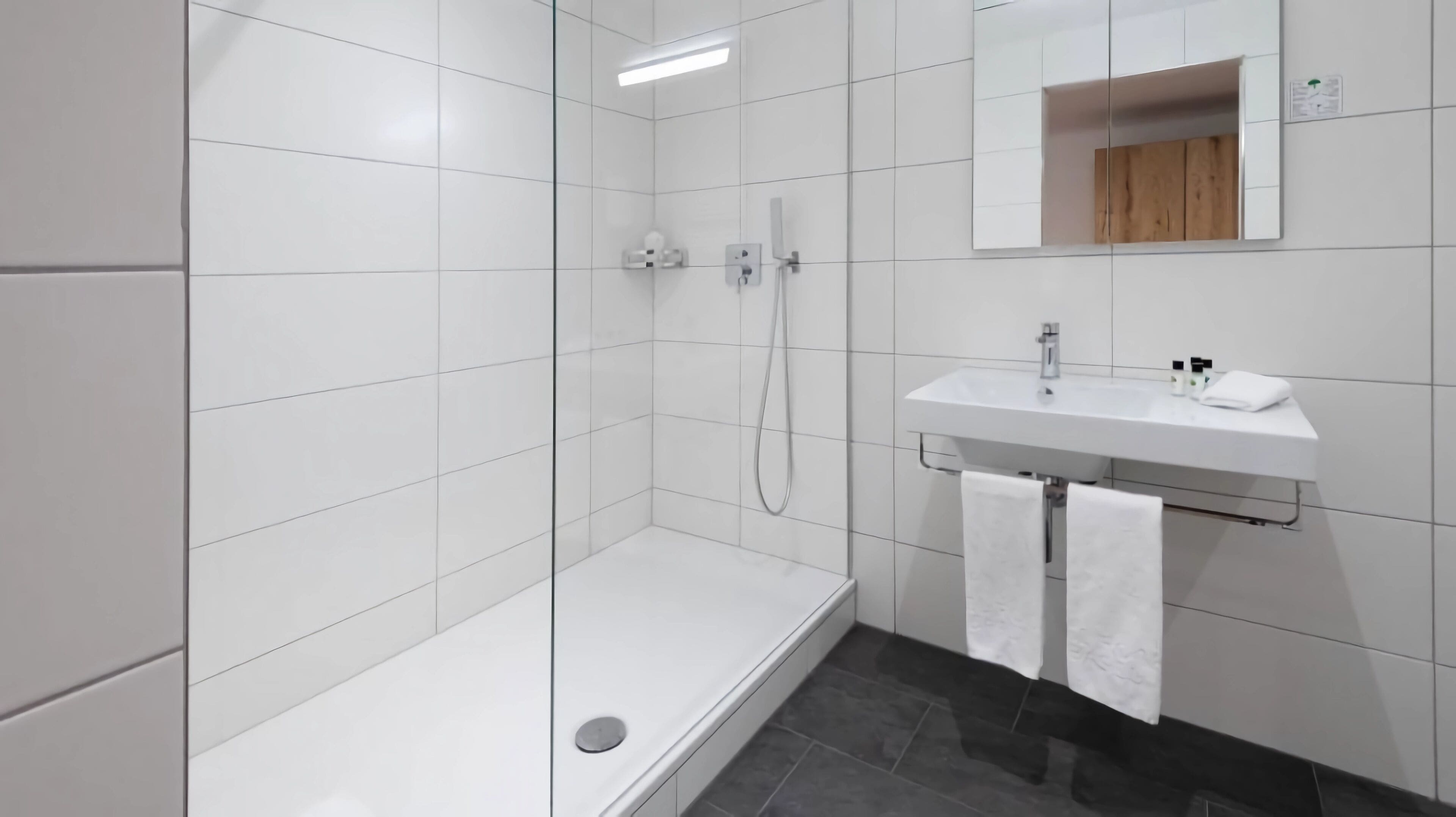 Un baño moderno con azulejos blancos, ducha, lavamanos y espejo.