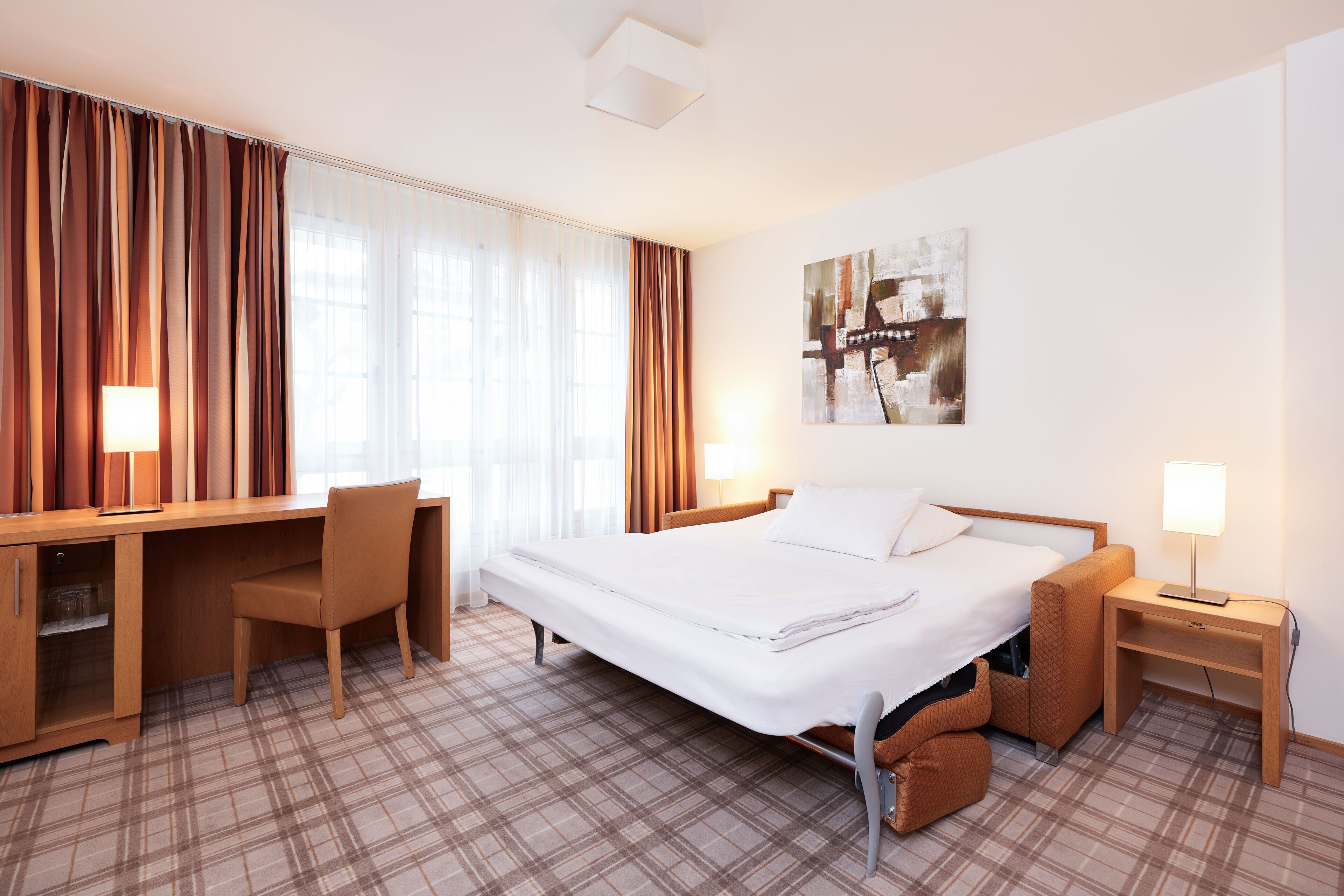 A hotel room with a bed, desk, chair, and a small seating area.