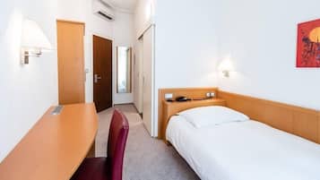 A hotel room with a single bed, a desk, a chair, and a small table.