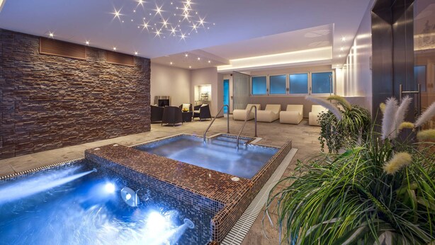 Un espace piscine intérieur moderne, avec un mur en pierre, des fauteuils confortables et un luminaire au plafond.