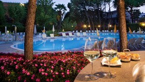 Un espace repas aménagé au bord de la piscine, avec une table dressée pour deux personnes, un verre de vin blanc et un panier de collations.