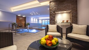 Un espace piscine intérieur moderne, avec un mur en pierre, des chaises longues et une table garnie de fruits.