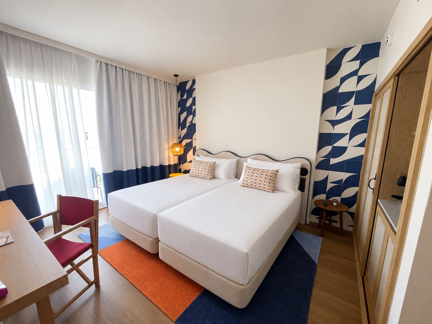 A hotel room with two beds, a desk, a chair, and a small table.