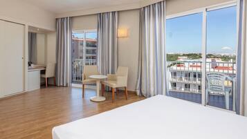 Ein Hotelzimmer mit Bett, Schreibtisch, Stuhl und Blick auf die Stadt durch große Fenster.