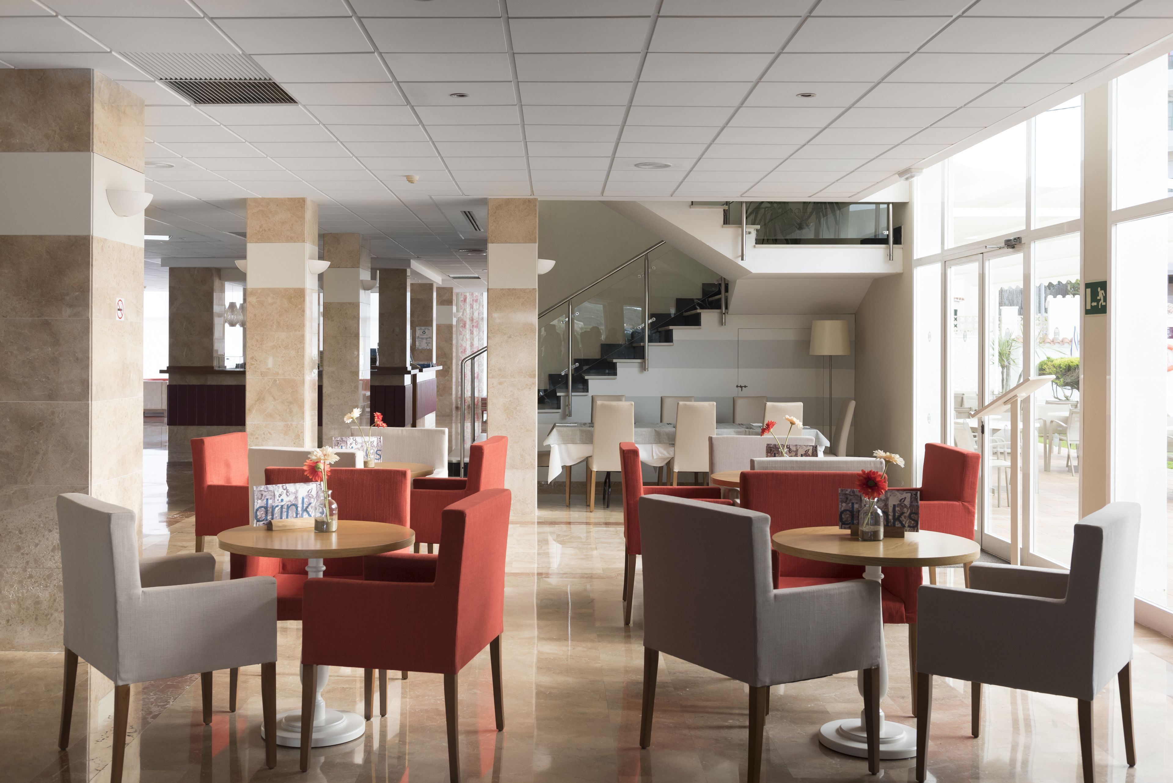 A modern hotel lobby with round tables and chairs, a staircase, and large windows.
