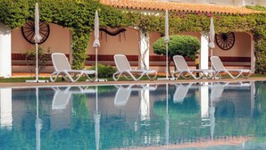 Una piscina con sillas de descanso blancas, techo de baldosas y follaje en las paredes.