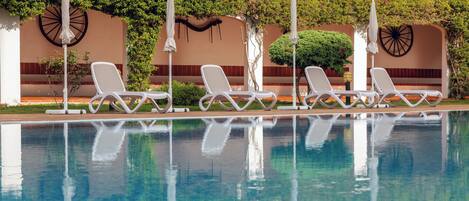 Ein Pool mit weißen Liegestühlen, einem Ziegeldach und Pflanzen an den Wänden.