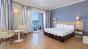 A hotel room with a bed, a small table, two chairs, a nightstand, and a view of the balcony.