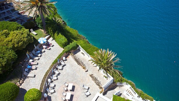 Vista aérea de un hotel frente al mar con zonas de estar al aire libre, palmeras y una vista despejada del océano.