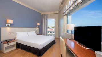 Habitación de hotel con cama, mesitas de noche, escritorio con silla, televisor y ventana con vistas.