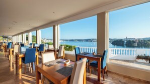 Un restaurante con terraza que da a un cuerpo de agua y un pueblo lejano.