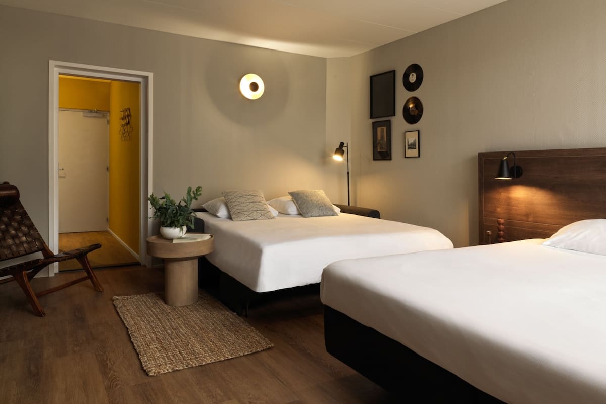 A hotel room with two beds, a bedside table, a lamp, and a small rug.