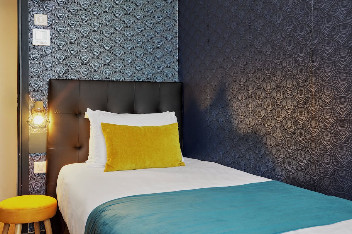A hotel room with a bed, a nightstand, and a wall with a patterned wallpaper.