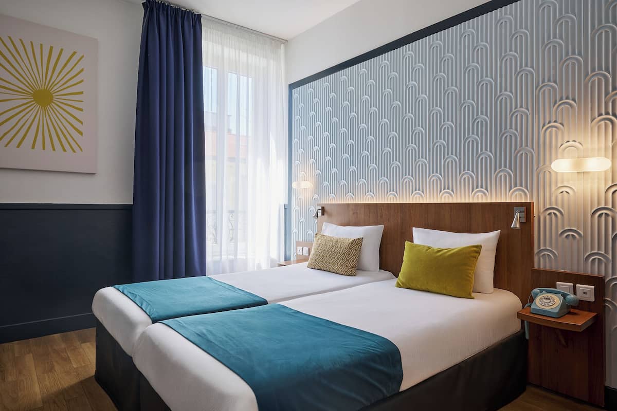 A double bed with a wooden headboard, two bedside tables, a telephone, and a window with curtains.