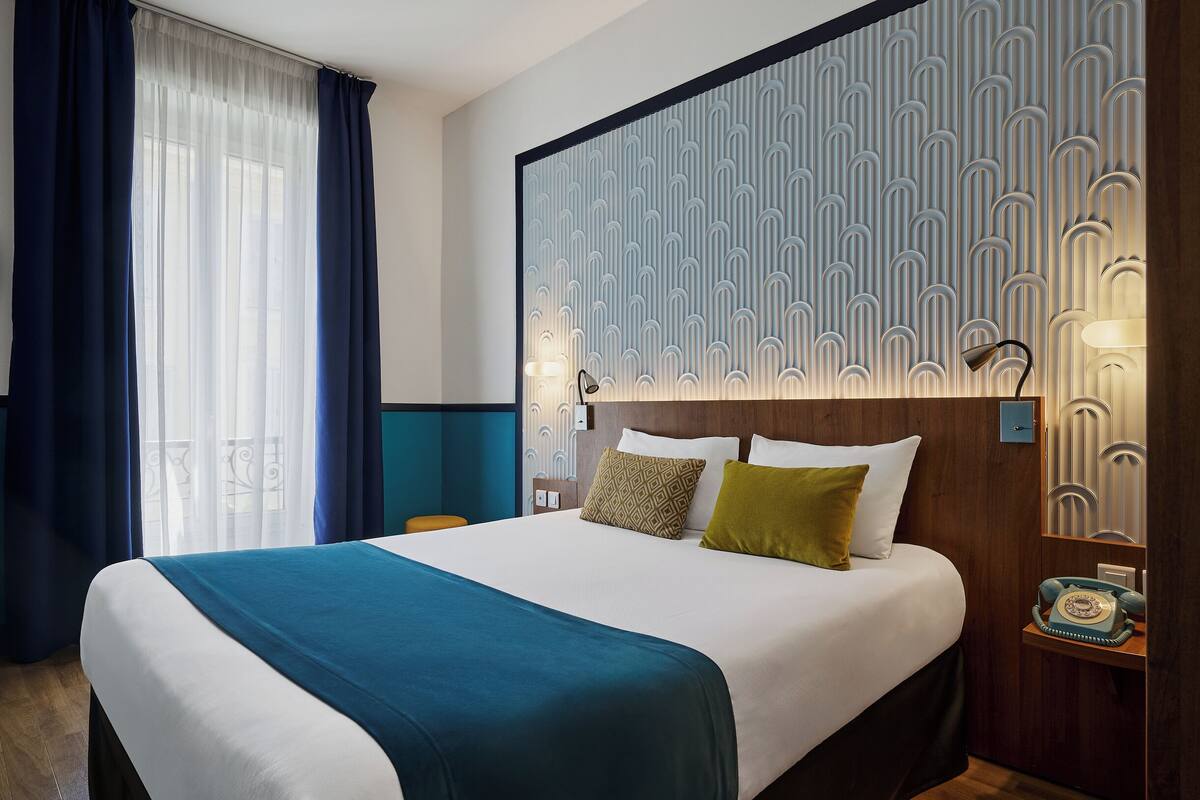 A hotel room with a large bed, a nightstand with a telephone, and a wall with a geometric pattern.