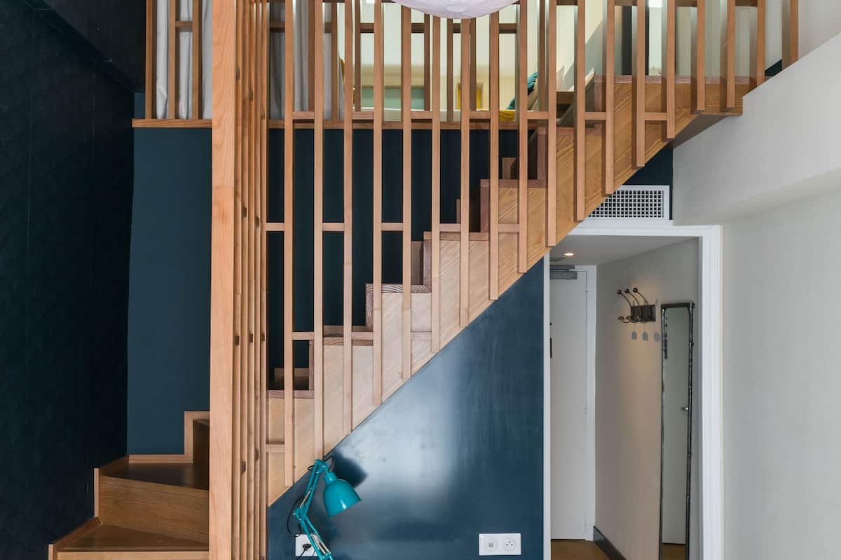 A modern interior with a wooden staircase, a desk with a chair, and a hanging light fixture.