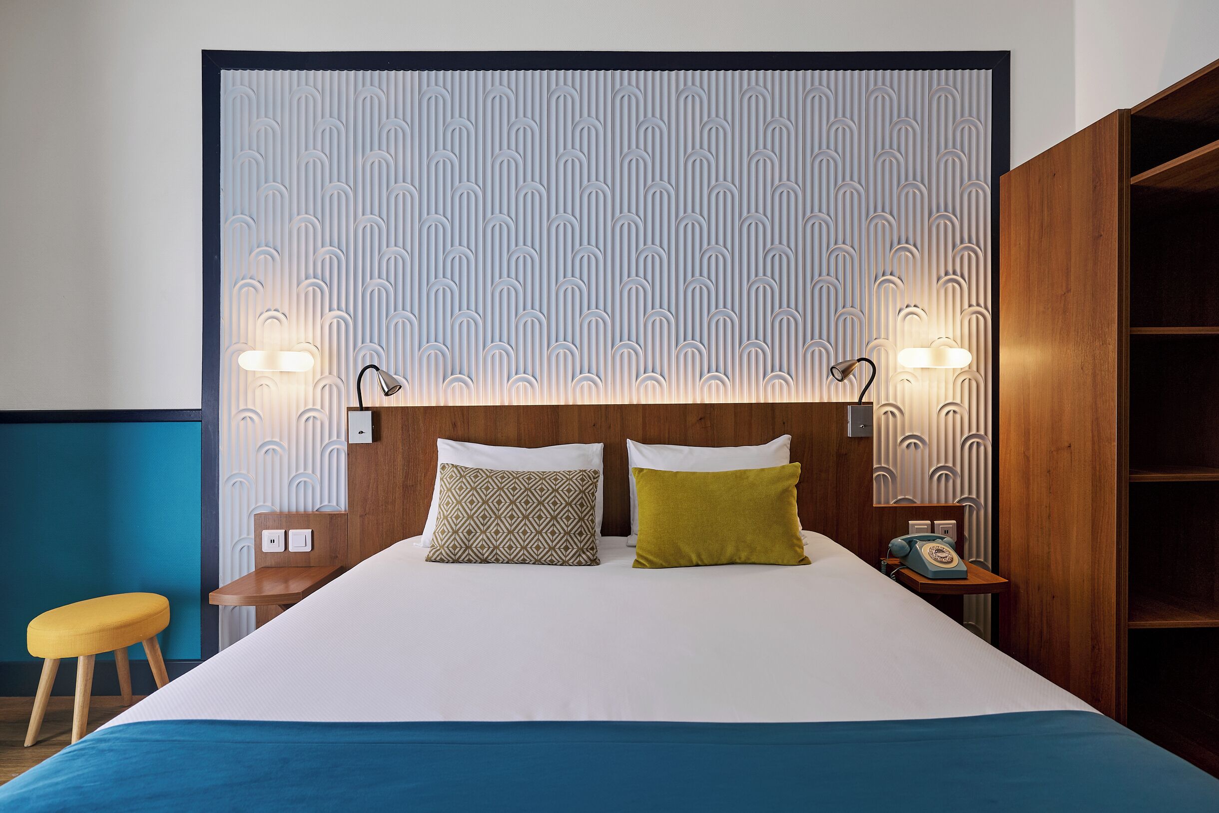 Una cama con dos almohadas, una mesita de noche con teléfono y una pared con diseño decorativo.