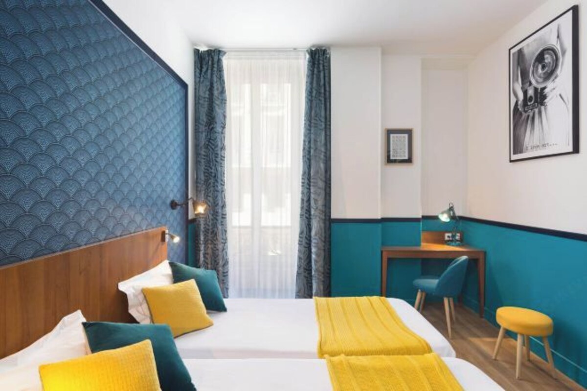 Une chambre d’hôtel avec deux lits, un bureau, une chaise et une fenêtre avec des rideaux.