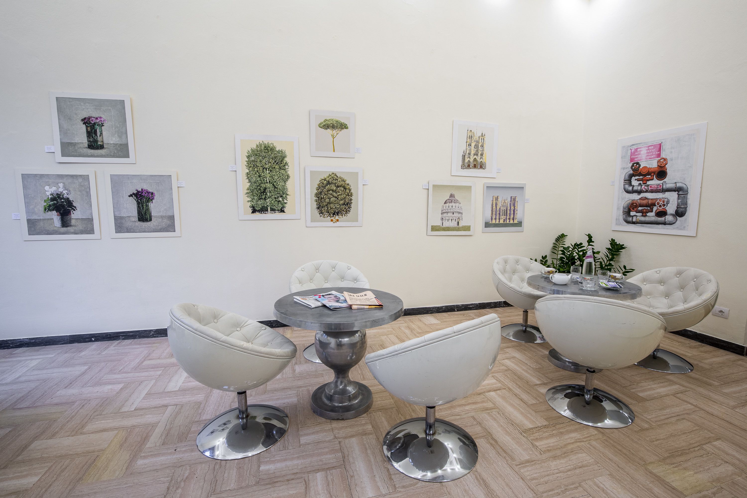 A room with a herringbone floor, four white chairs, a round table, and various framed artworks on the walls.