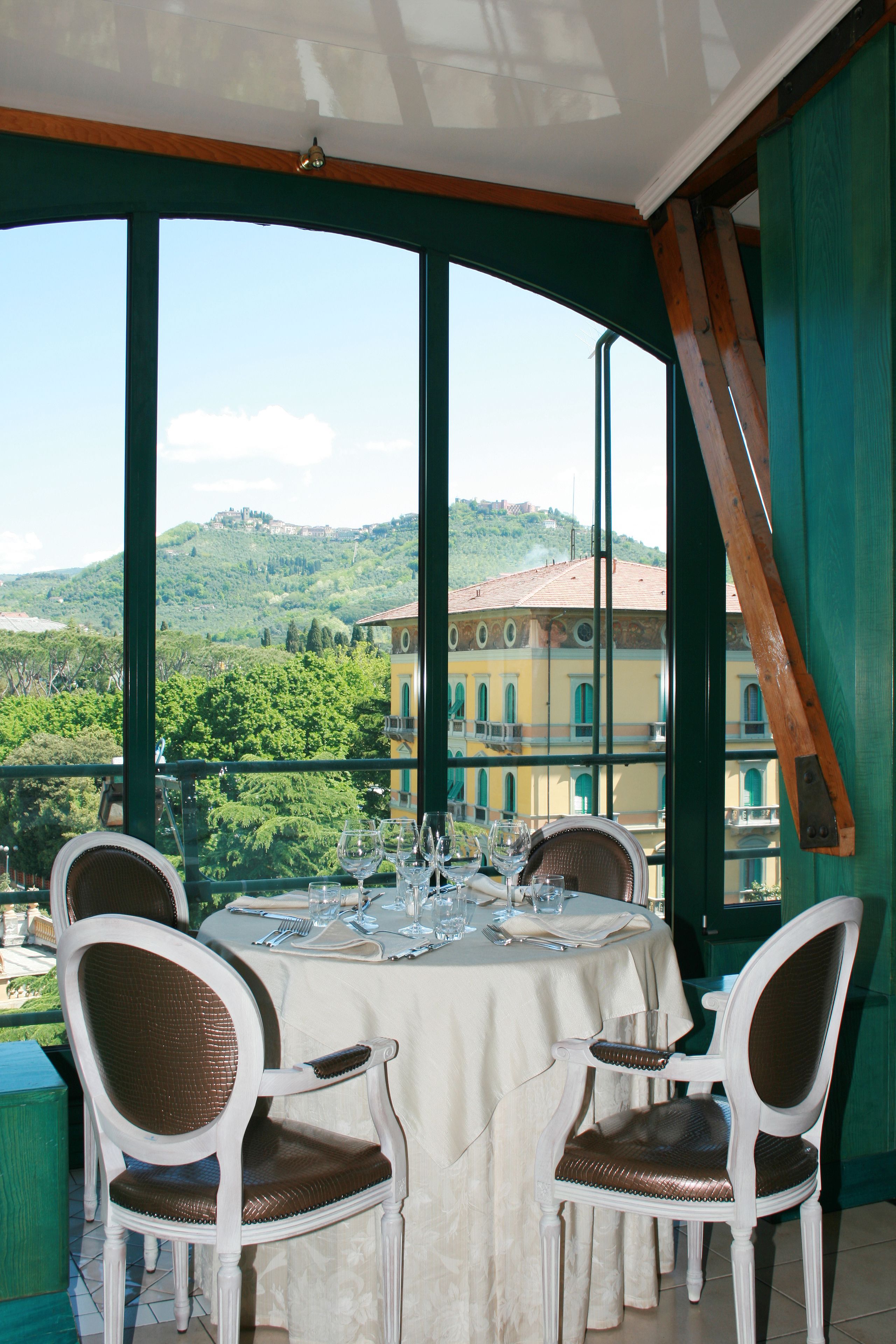 A dining table set with chairs, a view of a hill with buildings, and a wooden beam.