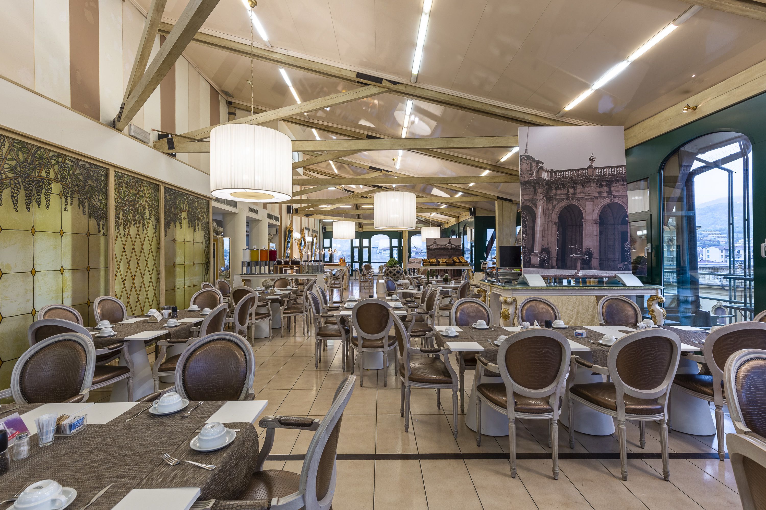 A spacious dining area with high ceilings and large windows, featuring a variety of seating arrangements and a central bar area.