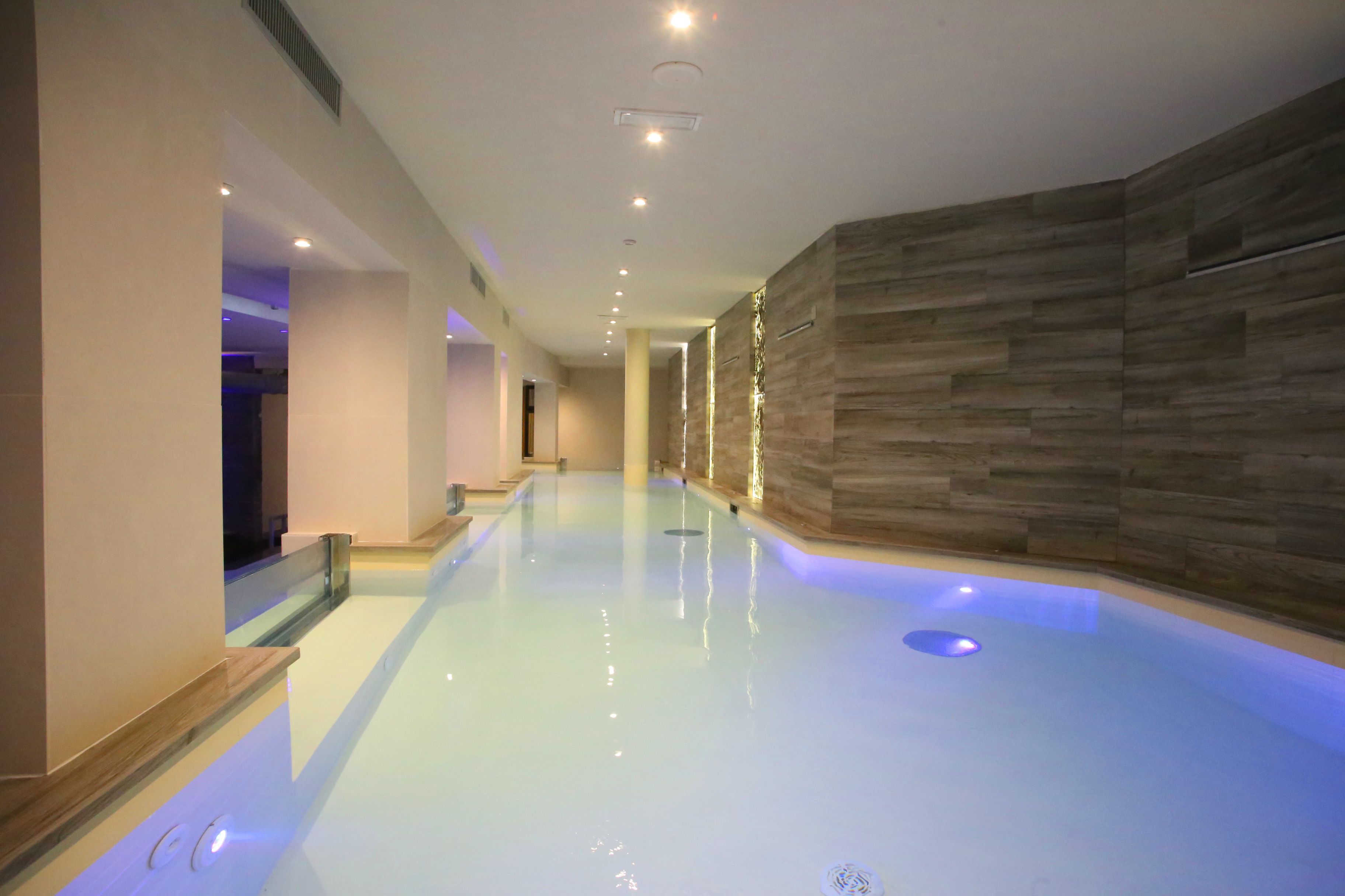 A modern indoor swimming pool with a clear water surface, surrounded by wooden panel walls and a glass railing.