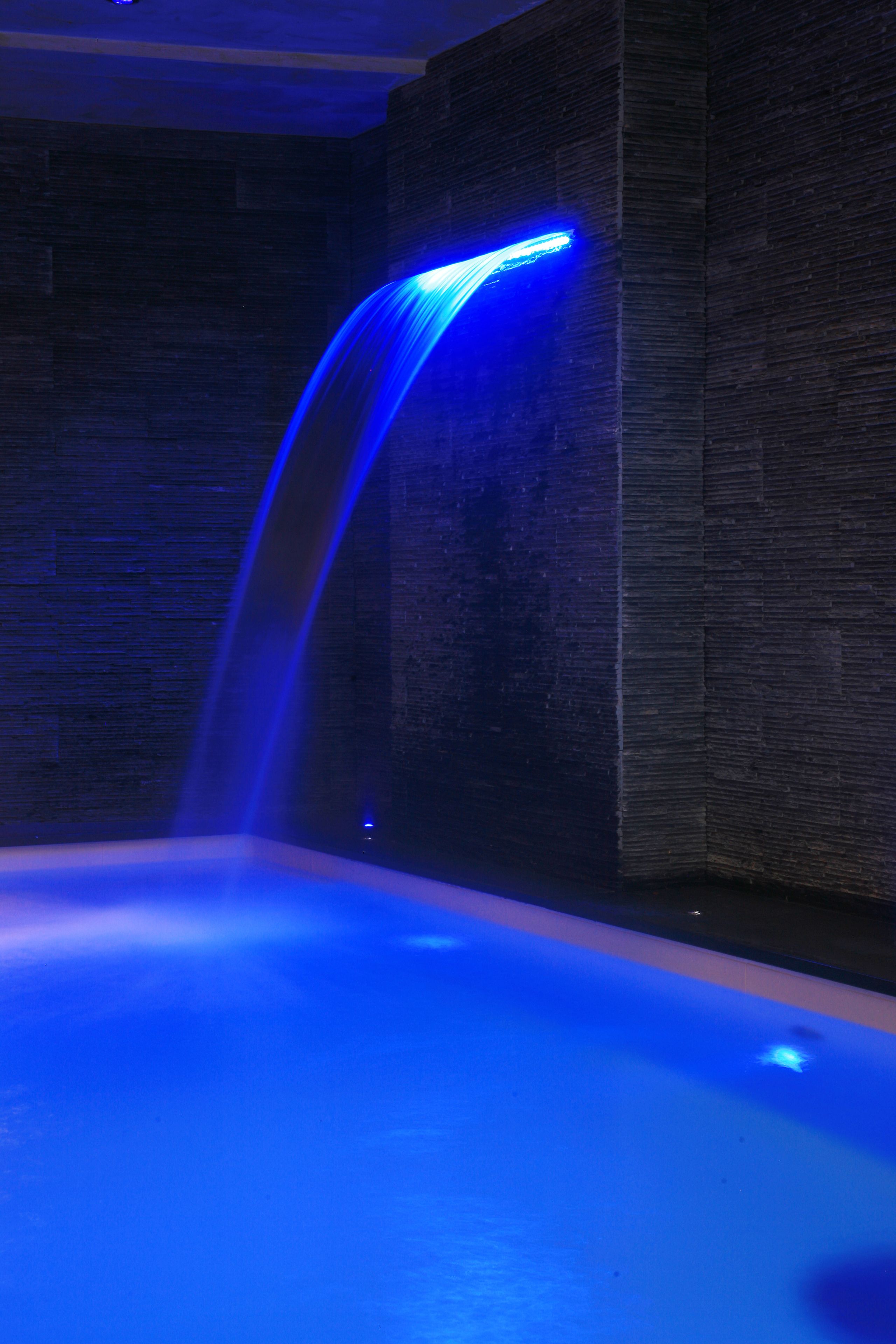 Zona de spa con fuente iluminada en azul y pared texturizada.