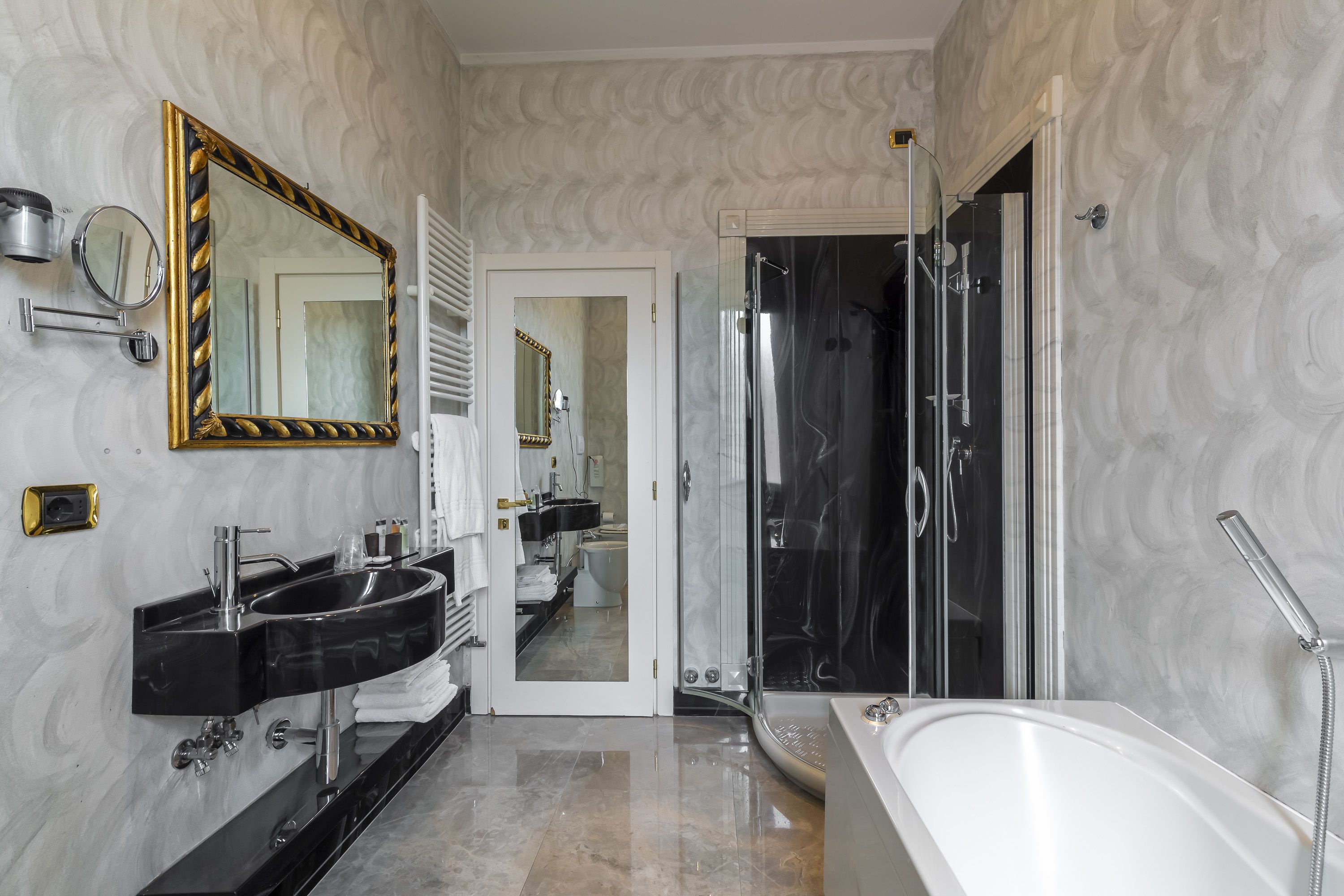 A modern bathroom with a large mirror, two sinks, a bathtub, and a shower area.