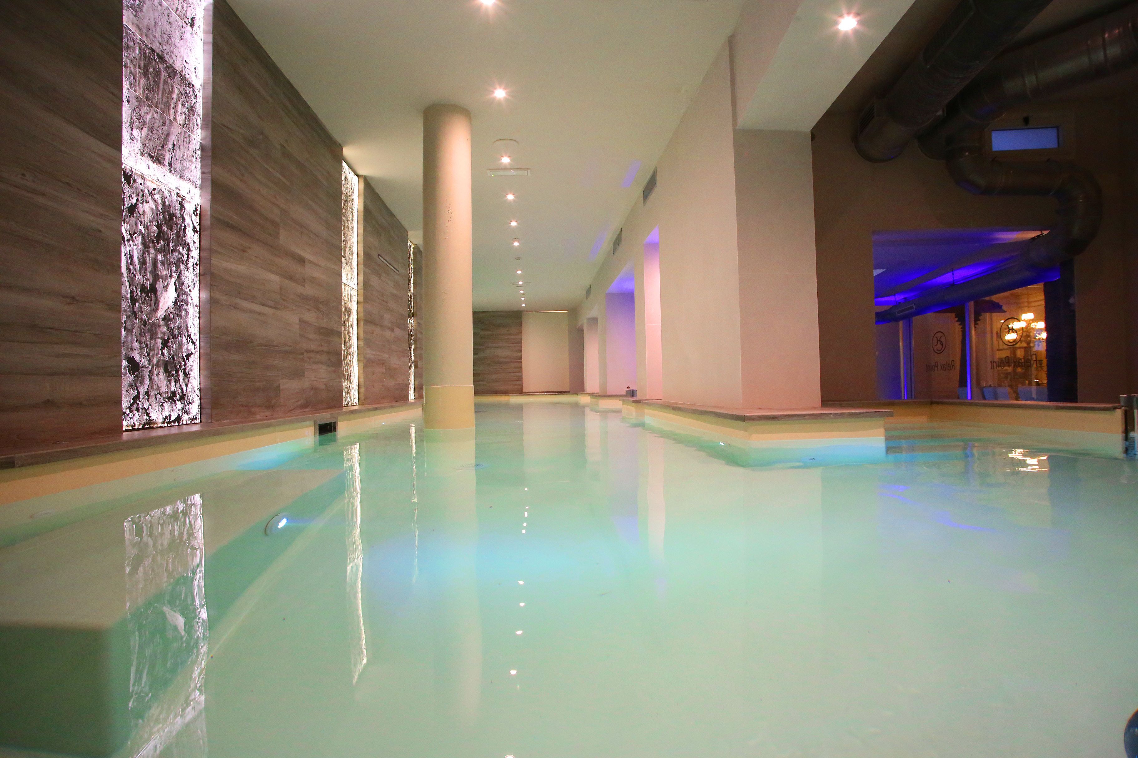 Ein geräumiger, überdachter Pool mit klarem Wasser, umgeben von Holzwänden und -säulen, und ein sichtbarer Zugang zu einem weiteren Bereich.