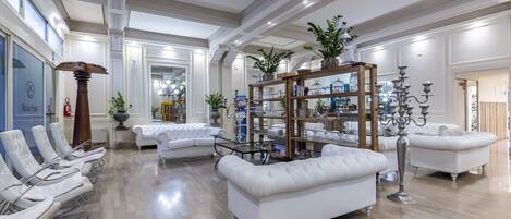 A spacious lobby with white leather sofas, a wooden bookcase, and a large chandelier.
