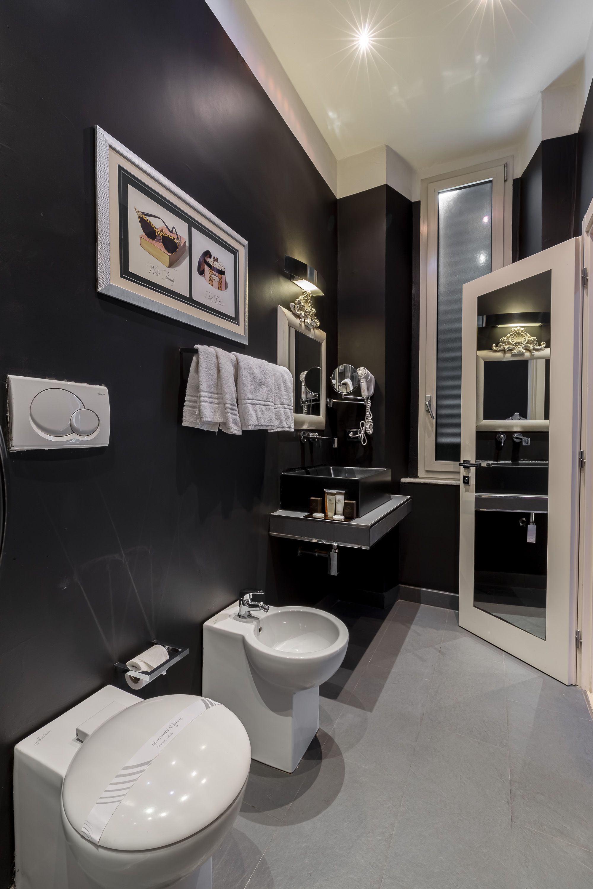 Un baño moderno con inodoro, bidé y tocador. Hay toallas colgadas en la pared y un cuadro enmarcado sobre el tocador.