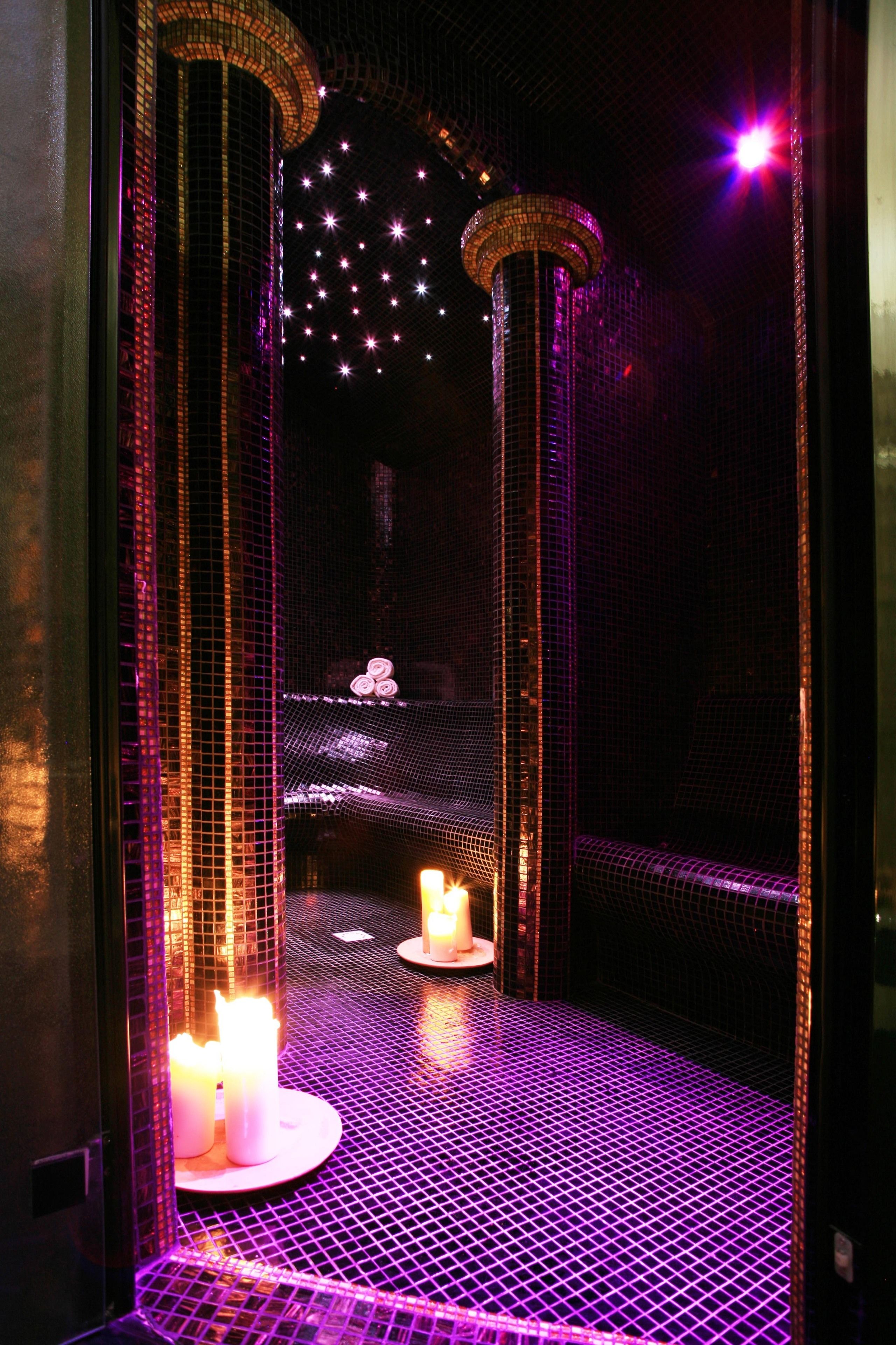 A dimly lit room with a patterned floor, a circular structure in the center, and candles on the floor.