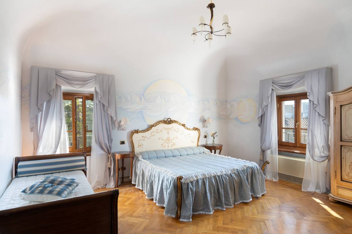 Un dormitorio con una cama grande, una araña y una ventana con cortinas.