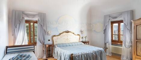 A bedroom with a large bed, a chandelier, and a window with curtains.