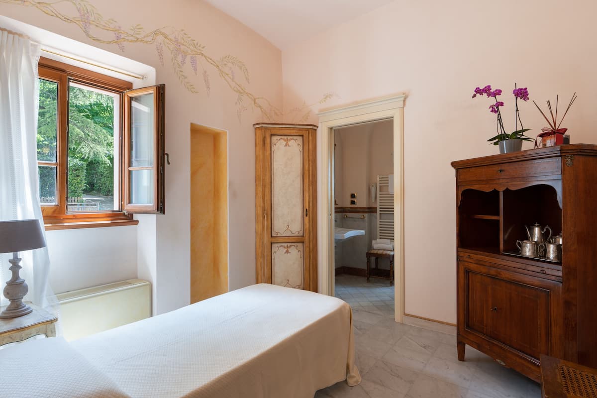 Un dormitorio con cama, cómoda, ventana con cortinas y vistas al baño.