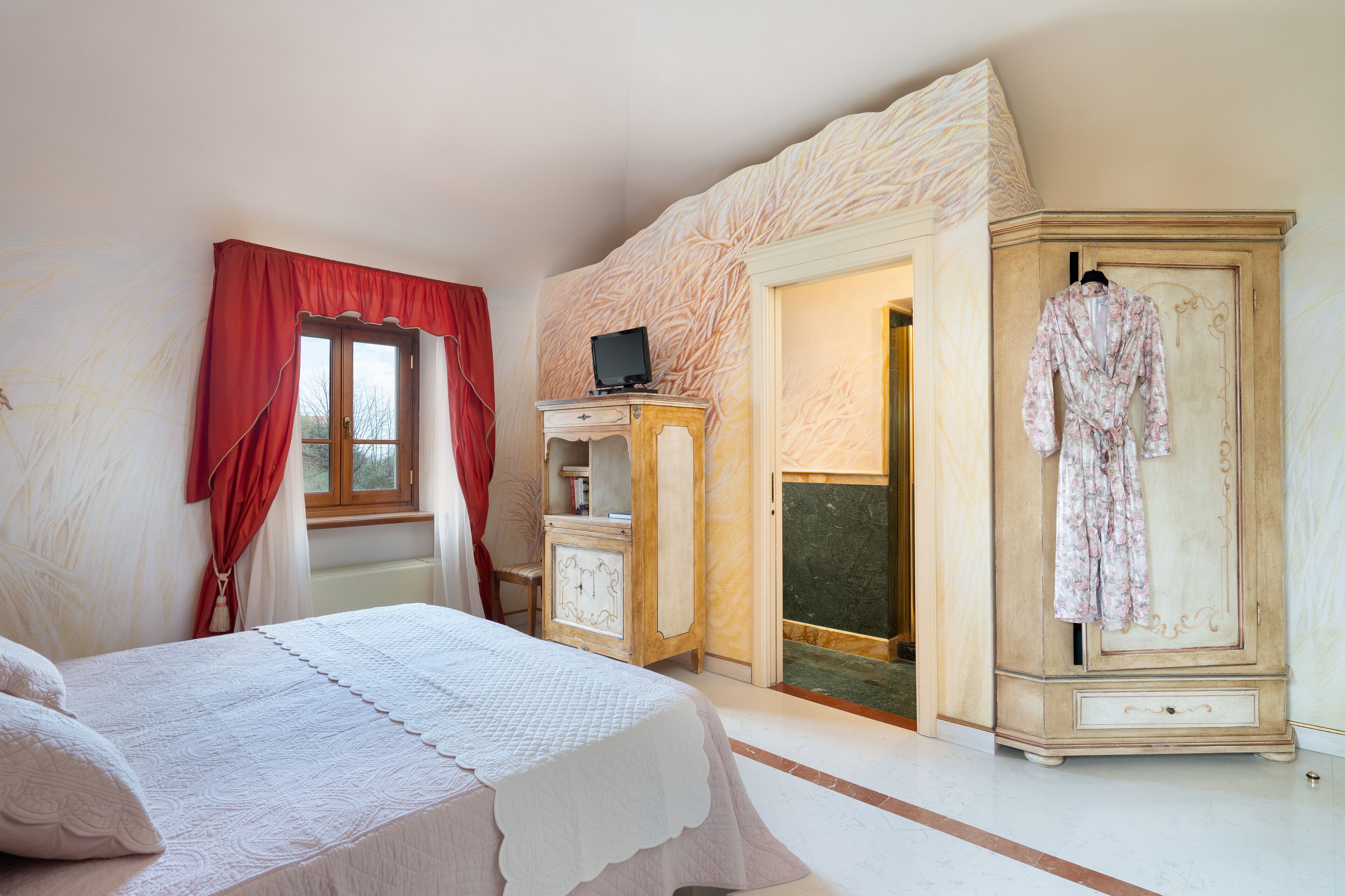 A bedroom with a bed, a wardrobe, a television on a cabinet, and a red curtain.