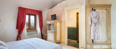A bedroom with a bed, a wardrobe, a television on a cabinet, and a red curtain.