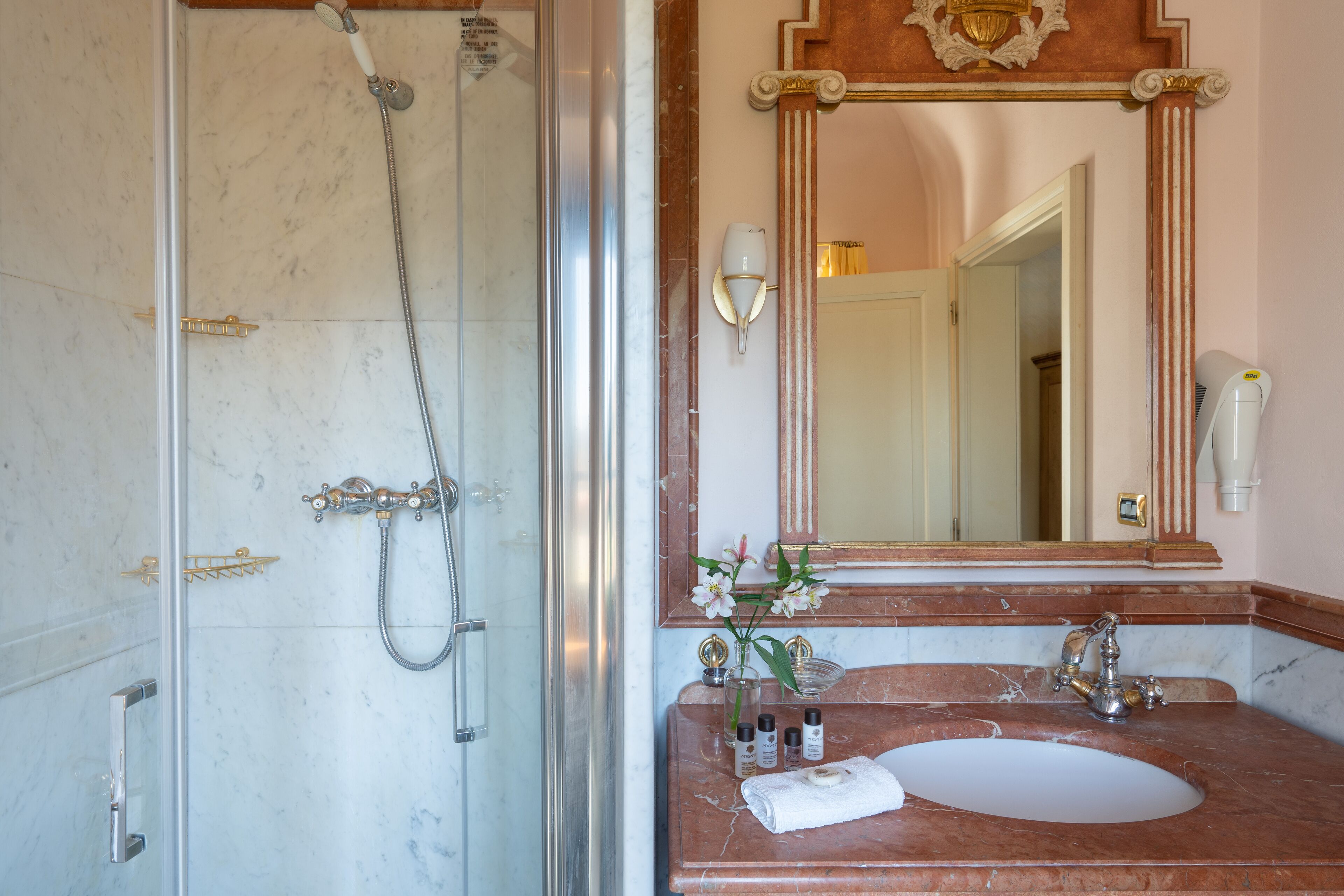 A bathroom with a glass-enclosed shower, a marble sink, and a large mirror with a decorative frame.