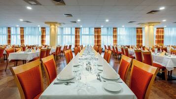 Une vaste salle de banquet, avec de longues rangées de tables dressées pour le repas, agrémentée de chaises orange et de nappes blanches.