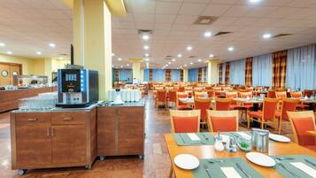 A large dining area with multiple tables and chairs, a coffee machine, and a buffet counter.