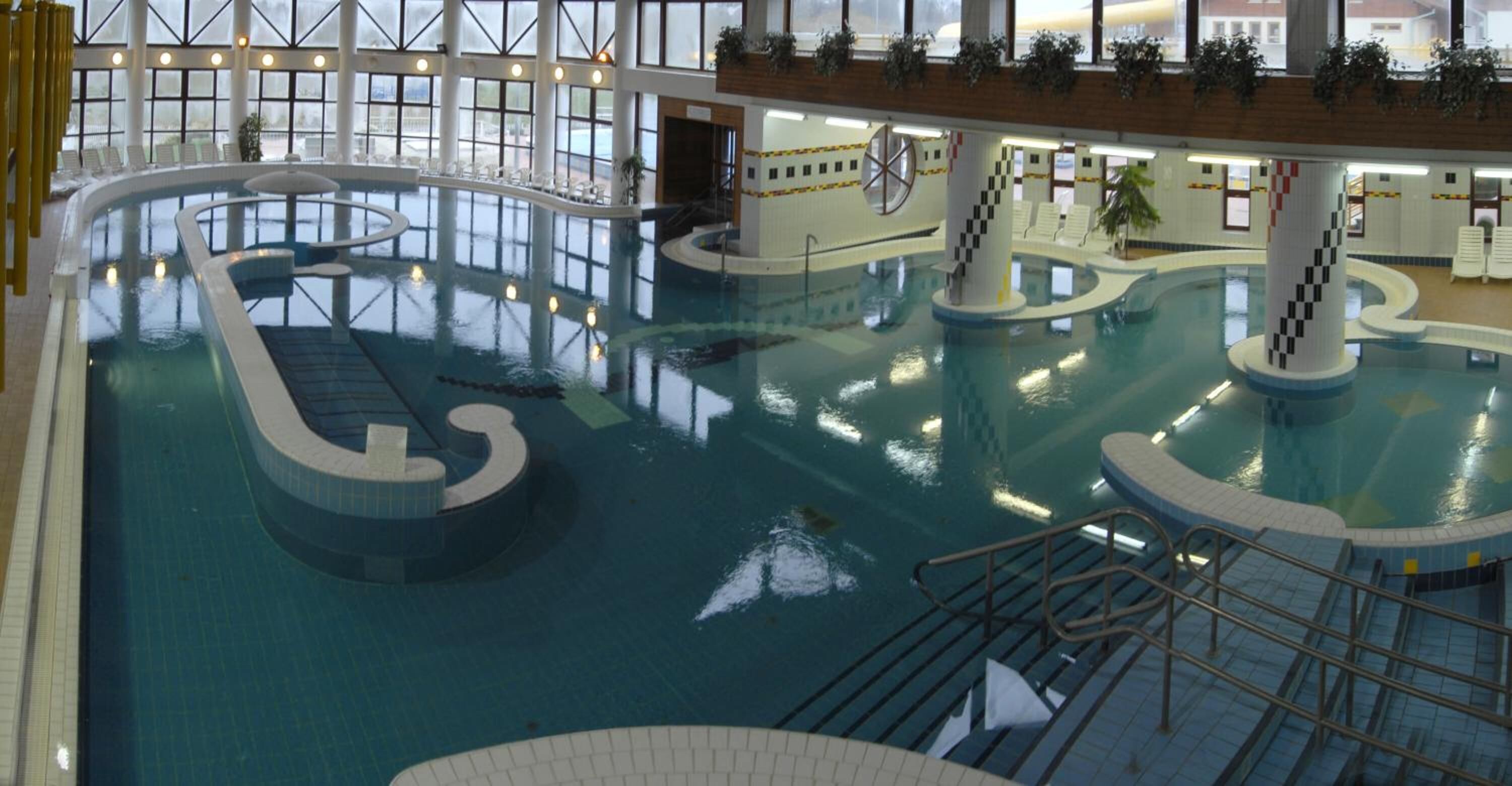 An indoor swimming pool with multiple lanes, a central island, and a viewing area with chairs.