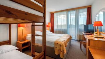Habitación de hotel con literas, un escritorio con lámpara, televisión y un ventanal grande con cortinas.