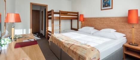 A hotel room with a bunk bed, a desk with a telephone, a remote control, and two lamps.