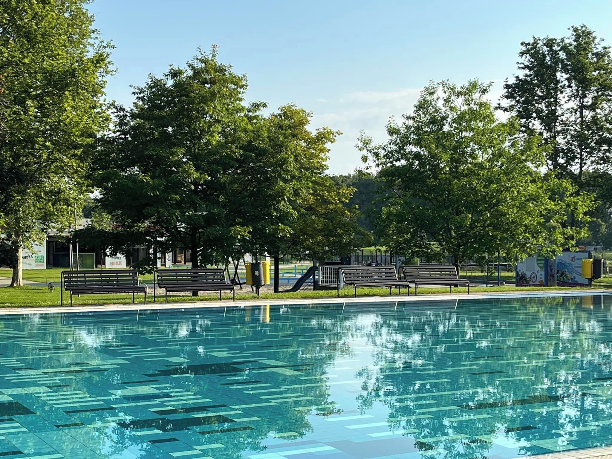 A swimming pool with benches and trees around it.