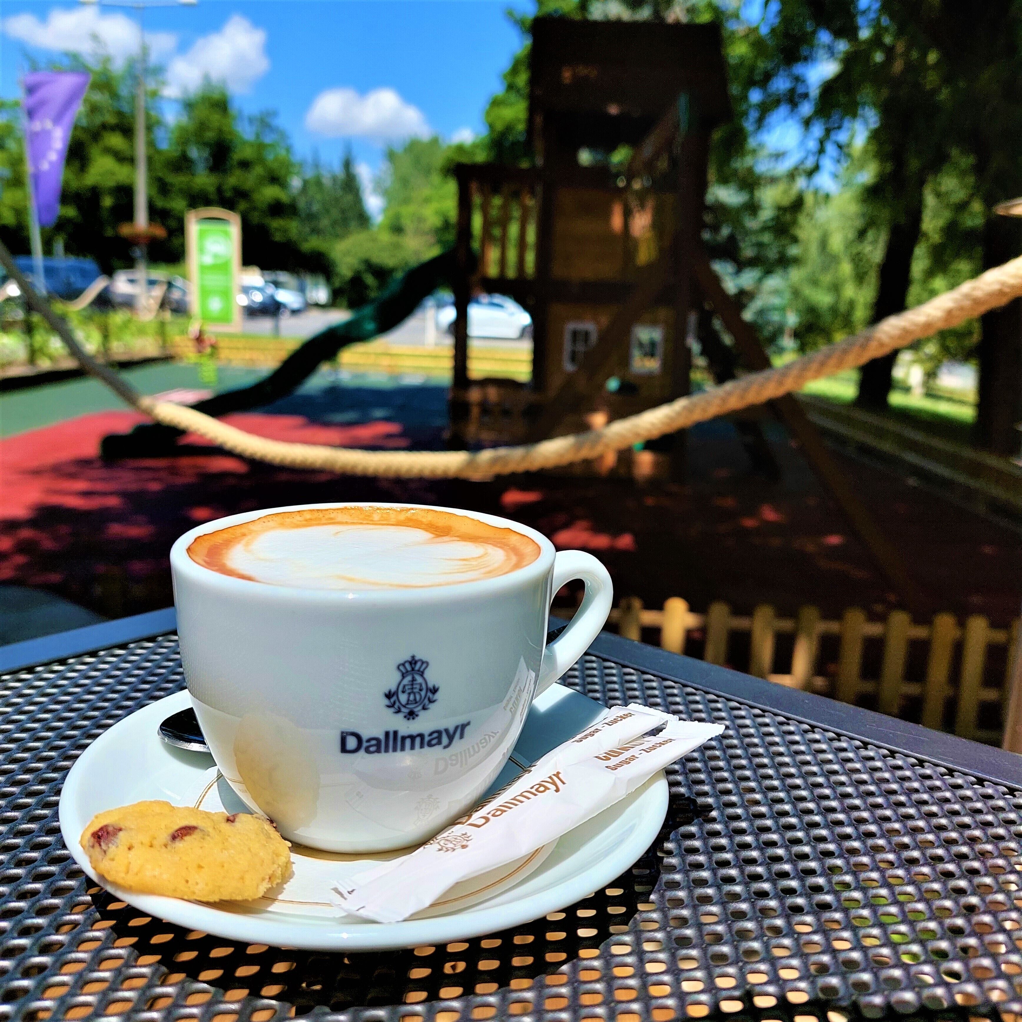 A cup of coffee with a biscuit on a metal table outdoors.