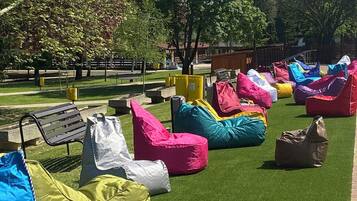Outdoor bean bag seating on artificial grass, surrounded by trees and a wooden fence.