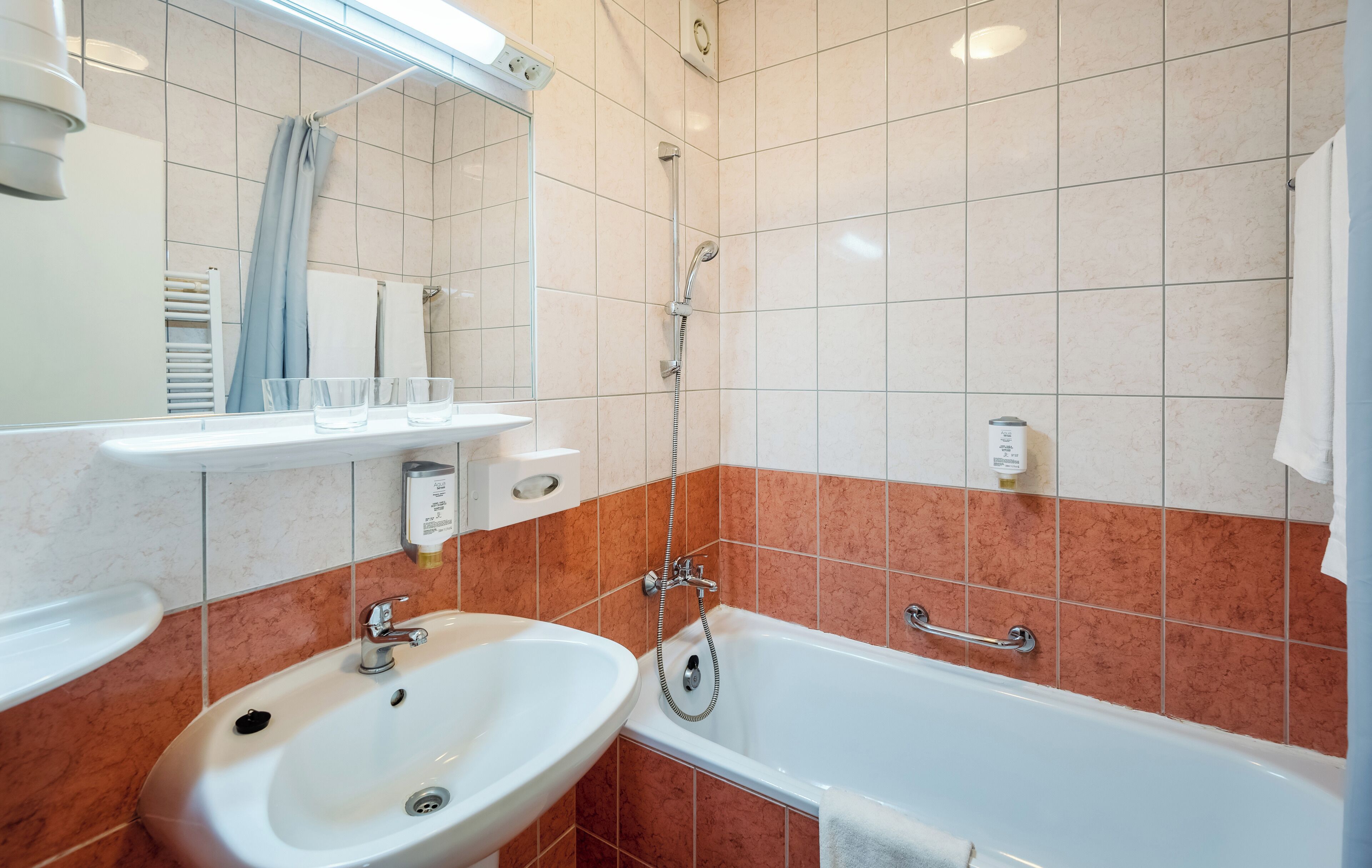 Baño con lavamanos, espejo, ducha y toallero.