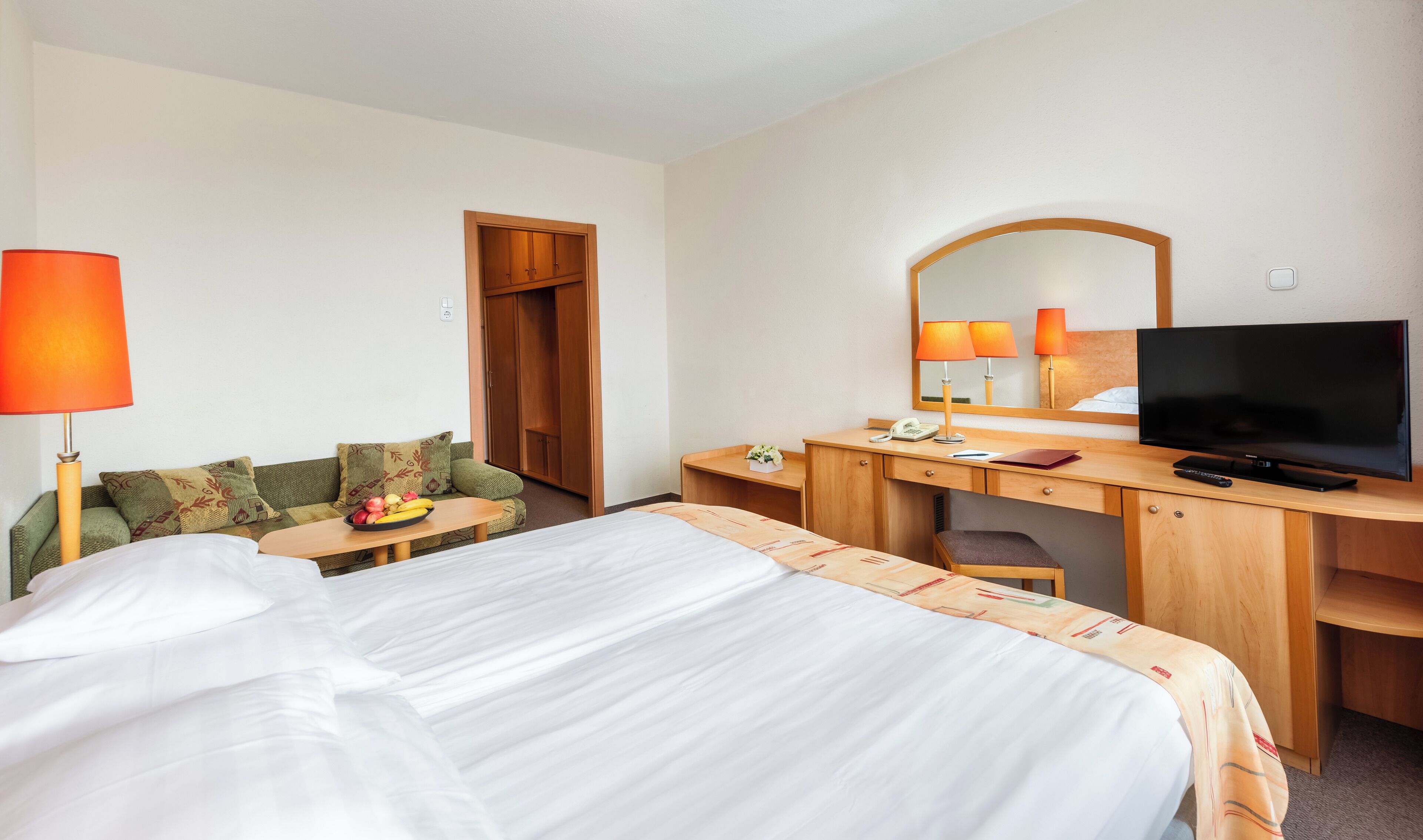 Een hotelkamer met een bed, een bureau, een televisie en een spiegel.